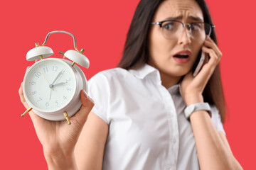 Stressed young woman with alarm clock on red background, closeup. Deadline concept