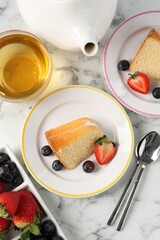 Pieces of tasty bundt cake with berries and tea on white marble table, flat lay