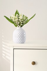 Beautiful lilies of the valley flowers in vase on chest of drawers