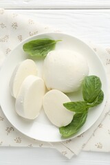 Pieces of delicious mozzarella cheese and basil on white wooden table, top view