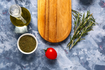 Wooden kitchen board, spices, rosemary and oil on color background