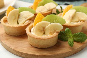Tartlets with fruits and mint on table, closeup. Delicious dessert