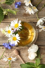 Aromatic herbal tea in glass cup, flowers and dipper on wooden table, flat lay