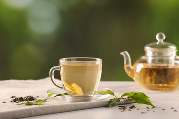 Cup of tasty green tea with lemon and teapot on light table against blurred background