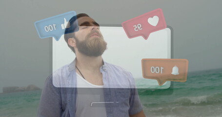 Standing bearded man wearing blue shirt and necklace over tee at sandy shore, with reaction bubbles