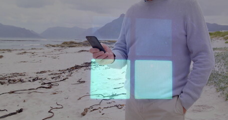 Using smartphone, man on beach interacting with image overlay on screen
