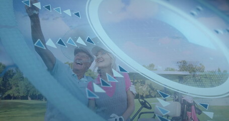 Pointing senior couple wearing gloves on fairway, with golf cart, smartphone and digital graphics