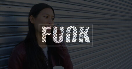 Asian woman in red jacket holding coffee cup using smartphone by storefront shutter, copy space