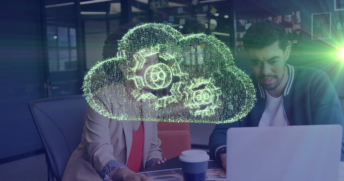 Tech colleagues collaborating at office with laptop cup, docs and holographic cloud icon with gears