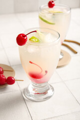 Glasses of tasty cocktail with maraschino cherries on white tile background