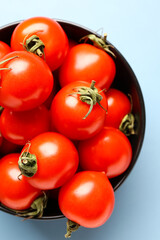 Bowl with fresh cherry tomatoes on blue background
