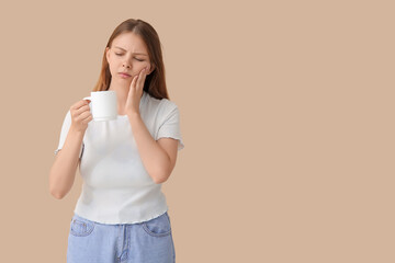 Young woman with sensitive teeth and cup of hot coffee on beige background