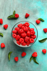 Glass bowl with fresh raspberries and mint on blue background