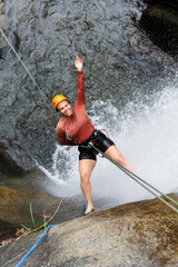 Latin american woman enjoying a thrilling canyoneering adventure, rappelling down a stunning...