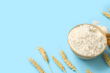 Bowls with wheat flour and spikelets on blue background