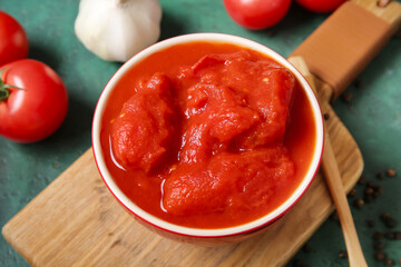 Wooden board with bowl of canned tomatoes on color background, closeup