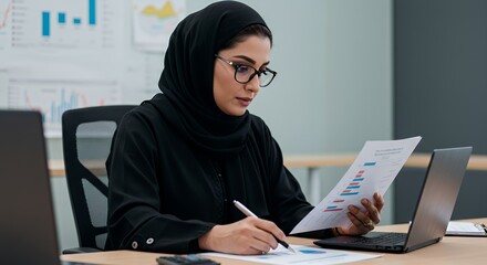 Focused Muslim businesswoman analyzes financial data at her desk.