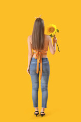 Fototapeta premium Young woman with beautiful sunflower on yellow background, back view