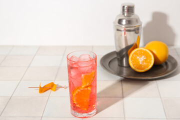 Glass of cold Negroni cocktail, oranges and shaker on light tile table