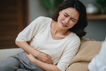 An empathetic photo illustrating digestive distress, where a woman curled up on a couch finds soothing relief from a warm compress for her stomach ache.