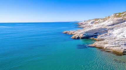 Aerial view of rocky coastline with clear blue water and gentle waves, showcasing natural beauty
