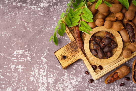 Wooden board and bowl of tasty tamarinds on grey background