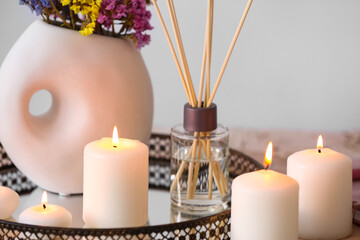 Tray with burning candles and reed diffuser on table