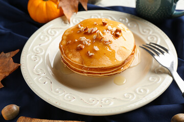 Plate of tasty pumpkin pancakes with honey and nuts on table