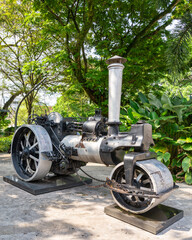 Vintage steamroller on display as a historical monument in Jalan Parlimen street by the Gombak River. Antique road construction machinery surrounded by lush tropical greenery