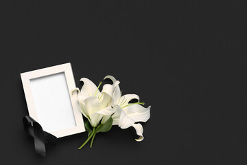 Beautiful lily flowers with blank frame and black funeral ribbon on dark background