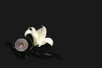 Beautiful lily flower with burning candle and black funeral ribbon on dark background