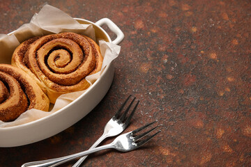 Baking dish of tasty cinnamon rolls on brown background