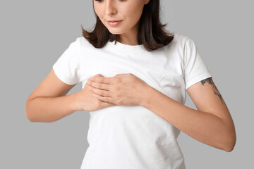 Young woman checking her breast on light background, closeup. Cancer awareness concept