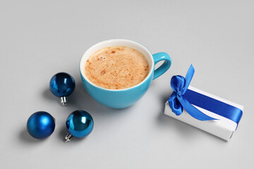 Cup of coffee with gift box and Christmas balls on grey background