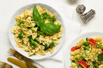 Plates of tasty pasta with broccoli and tomatoes on white background