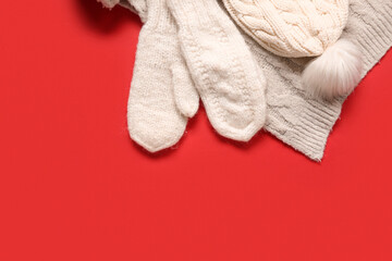 Pair of knitted mittens with warm hat and scarf on red background