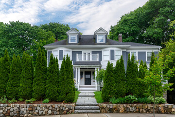 classic two-story family home surrounded by tall evergreens and leafy trees in Newton,...