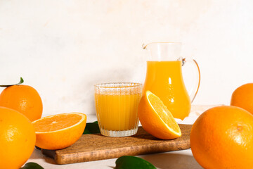 Wooden board with glass and jug of fresh orange juice on white background