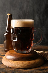Mug and bottle of cold dark beer with wheat on wooden table against black grunge background