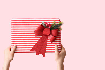 Female hands holding Christmas gift box on pink background