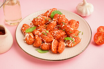 Plate of tasty gnocchi with cheese on pink background
