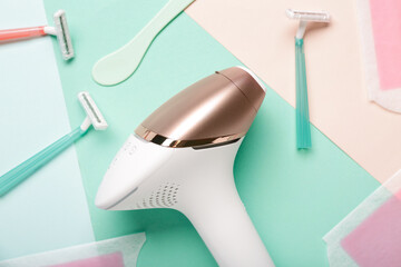 Modern photoepilator with razors and wax strips on color background