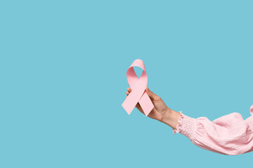 Female hand with pink ribbon on blue background. Breast cancer awareness concept