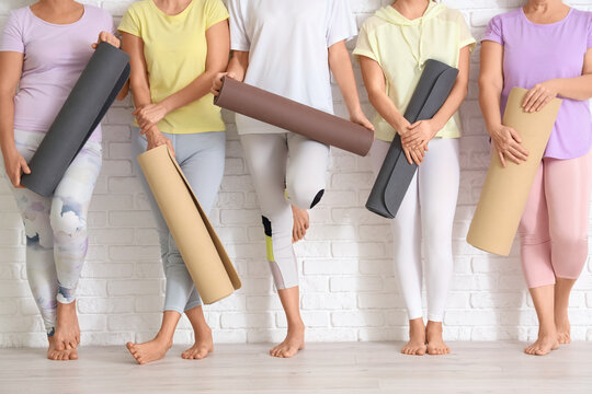 Group of mature women with yoga mats near white brick wall