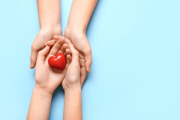 Hands of woman and child holding red heart on blue background