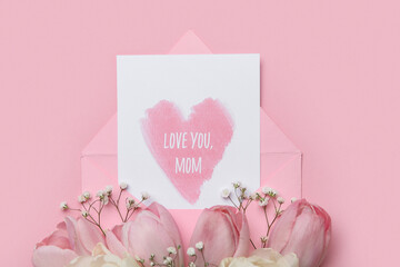 Envelope with festive postcard and flowers on pink background. Mother's Day celebration
