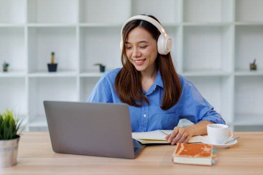 Focused Smiling girl student wearing headphones taking notes while listening to an online class on her laptop distant education
