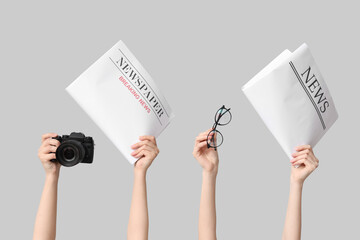 Female hands with newspapers, photo camera and eyeglasses on grey background