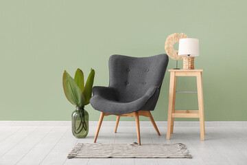 Black armchair, coffee table with lamp and plant in vase near green wall