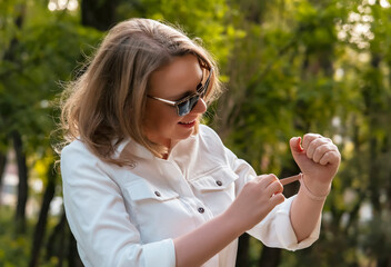 Woman enjoys a summer walk outdoors while checking her fitness bracelet and smiling in a park
